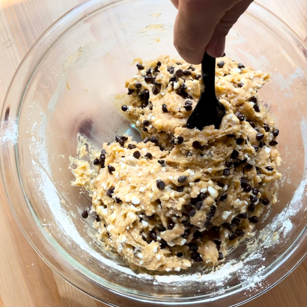 Chocolate chips being mixed into muffin batter in glass bowl 