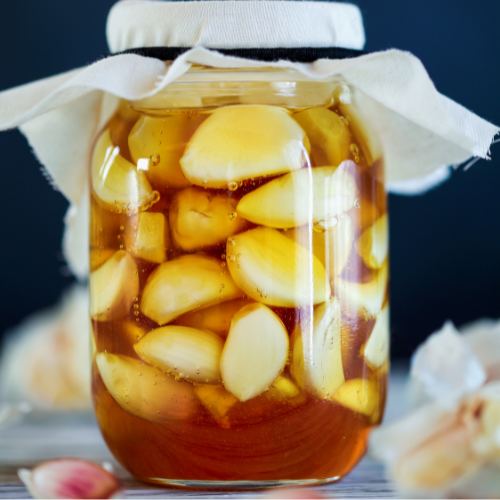 garlic honey fermented in glass gar with white cloth over