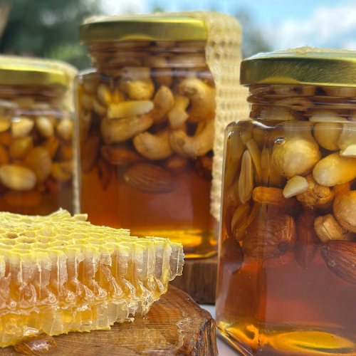 Three jars of fermented garlic honey next to honeycomb on table