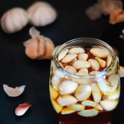 raw galic floating inside raw honey in glass gar on black surface